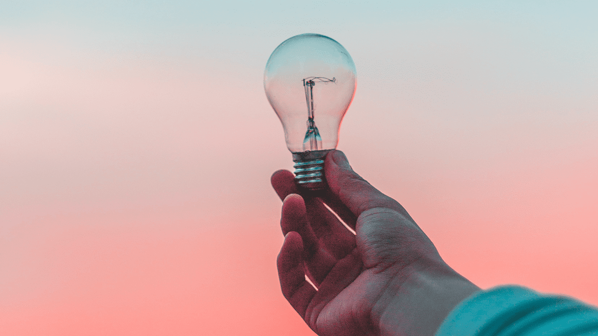 Person holding a lightbulb in front of a hazy pink-blue backdrop